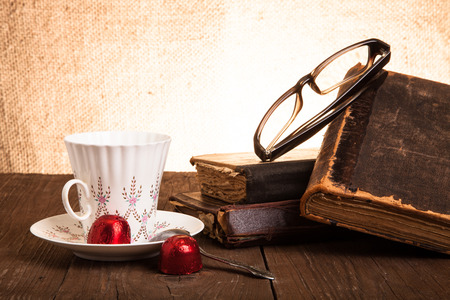 Cup of coffee, shokolad, glasses and stack of old books on the old wooden table.の写真素材