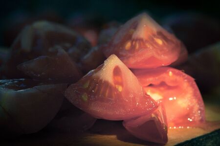 Pieces of tomatoes on a wooden board. Low light and shallow depth of field. Toned.の写真素材