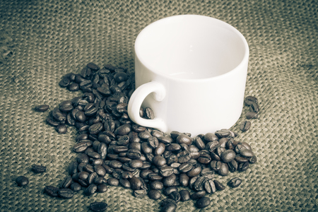 Coffee beans and an empty white cup on sacking background.の写真素材