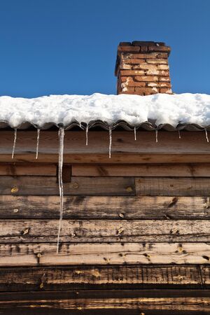 Brick chimney on the snow-covered roof of a wooden house.の写真素材