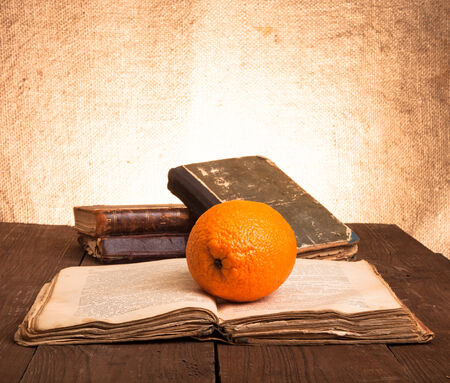 Still life with orange and old books on old wooden table. One of books is openedの写真素材