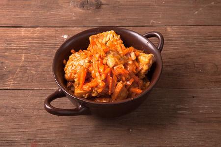 Fish marinated with carrots in a brown ceramic bowl on old wooden table.の写真素材