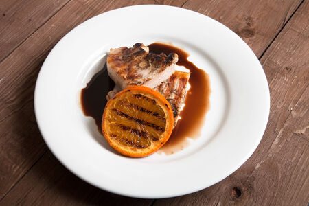 Grilled meat with orange on white ceramic plate on old wooden table.の写真素材