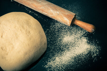 Dough, rolling pin and flour on a black background. Toned.の写真素材