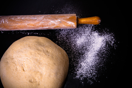 Dough, rolling pin and flour on a black background. Toned.の写真素材