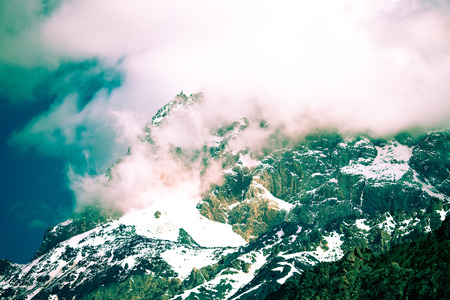 Clouds lie on the snow-covered tops of the rocks. Landscape. Toned.の写真素材
