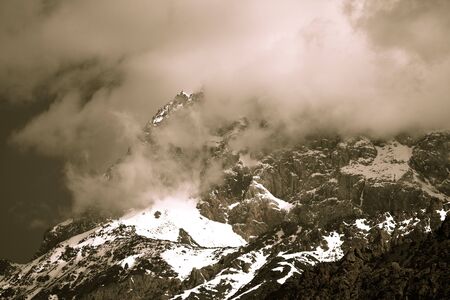 Clouds lie on the snow-covered tops of the rocks. Landscape. Toned.の写真素材