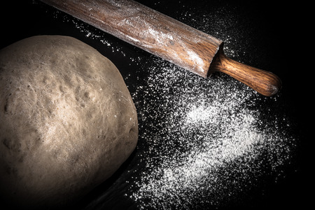 Dough, rolling pin and flour on a black background. Toned.の写真素材