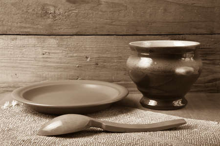 Rustic still life. Clay pot, spoon and plate on linen napkin. Wooden background. Toned.の写真素材