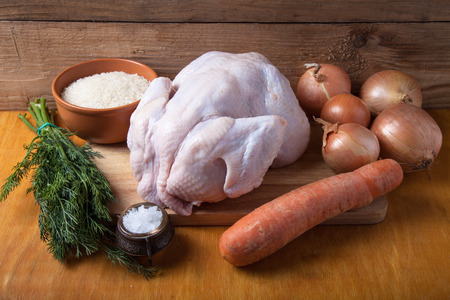 Whole raw chicken, onion, carrot, dill, rice, salt on wooden background. Rustic still life.の写真素材
