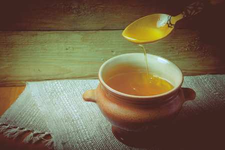 Clay pot with ghee and spoon on linen napkin. Rustic still life. Wooden background. Toned.の写真素材