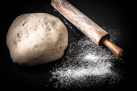 Dough, rolling pin and flour on a black background. Toned.の写真素材