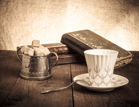Cup of coffee, sugar bowl and stack of old books on the old wooden table.の写真素材