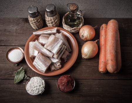 Pieces of fresh fish on a plate, vegetables, flour, tomatoe paste and spices on a wooden board. Toned.の写真素材