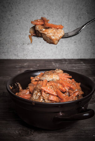 Fish marinated with carrots in a brown ceramic bowl and on the fork on old wooden table. Toned.の写真素材