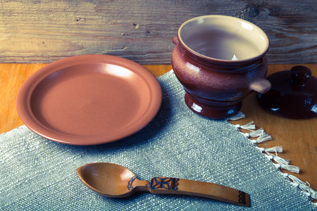 Rustic still life. Clay pot, spoon and plate on linen napkin. Wooden background. Toned.の写真素材