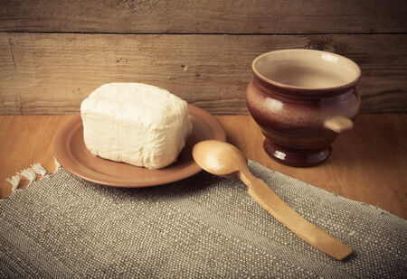 Butter on plate, clay pot and spoon on linen napkin. Rustic still life. Wooden background. Toned.の写真素材