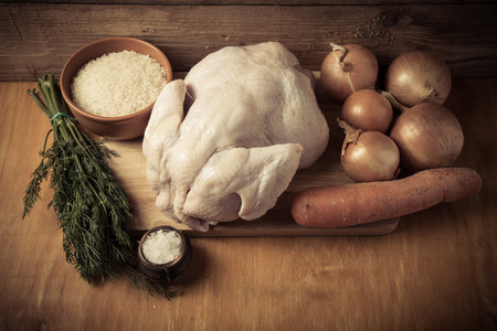 Whole raw chicken, onion, carrot, dill, rice, salt on wooden background. Rustic still life. Toned.の写真素材
