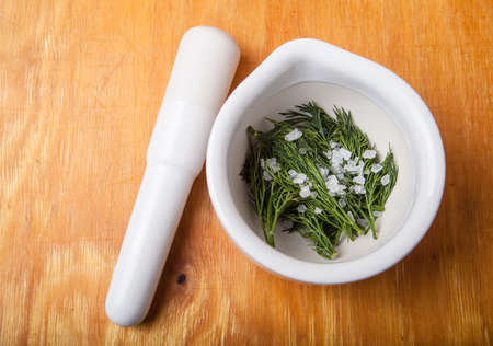 mortar with pestle and dill and salt on a wooden table.の写真素材