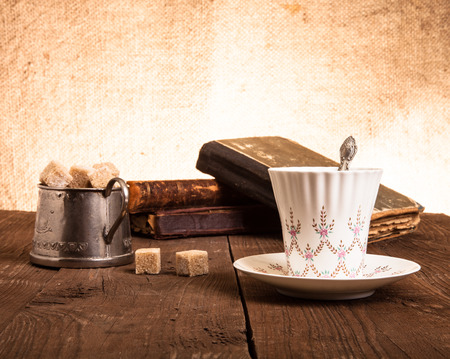 Cup of coffee, sugar bowl and stack of old books on the old wooden table.の写真素材