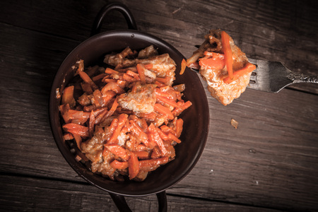 Fish marinated with carrots in a brown ceramic bowl and on the fork on old wooden table. Toned.の写真素材
