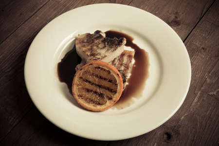 Grilled meat with orange on white ceramic plate on old wooden table. Toned.の写真素材