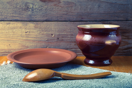 Rustic still life. Clay pot, spoon and plate on linen napkin. Wooden background. Toned.の写真素材