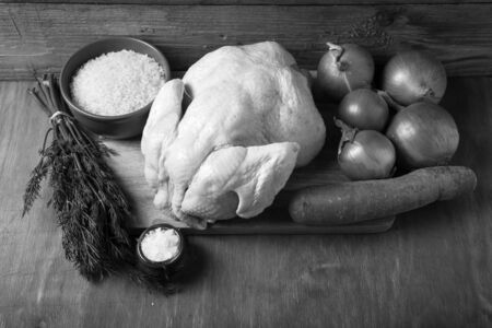 Whole raw chicken, onion, carrot, dill, rice, salt on wooden background. Rustic still life. Toned.の写真素材