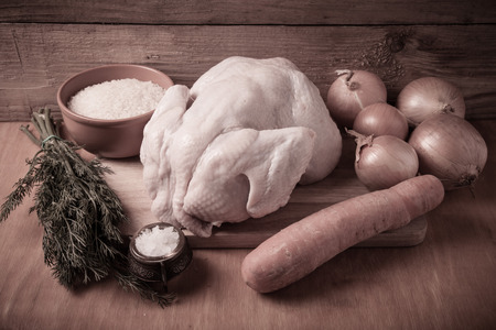Whole raw chicken, onion, carrot, dill, rice, salt on wooden background. Rustic still life. Toned.の写真素材