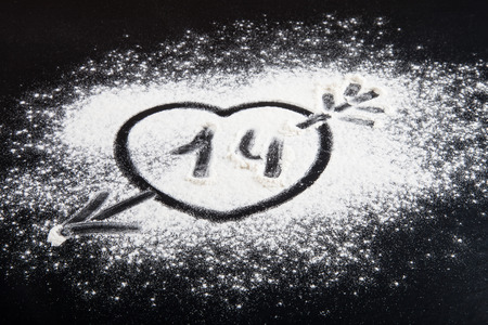 Shape of heart with arrow drawn on the flour on a black background.の写真素材