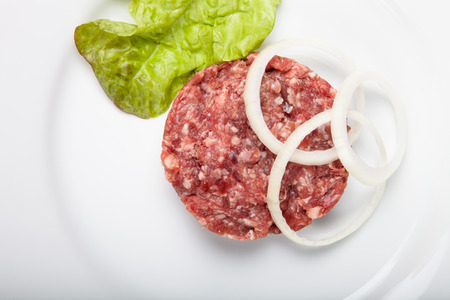 Raw steak with onion rings and green salad on a white plate.の写真素材