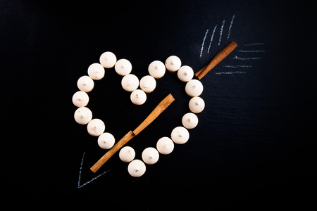 Small cookies laid in the shape of heart with arrow and cinnamon on black background.