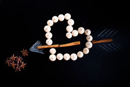 Small cookies laid in the shape of heart with arrow and cinnamon on black background.の写真素材