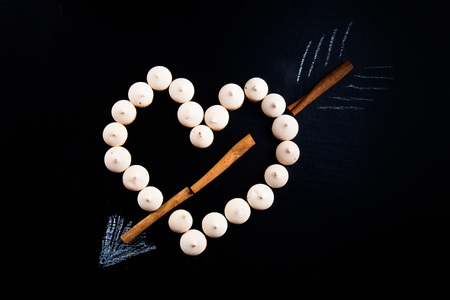 Small cookies laid in the shape of heart with arrow and cinnamon on black background.の写真素材