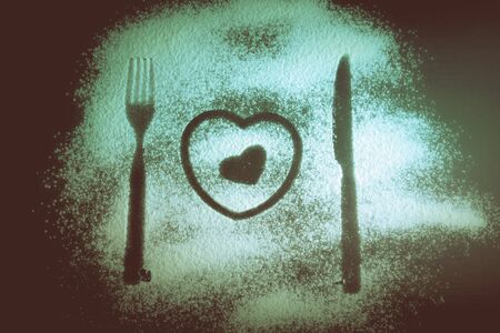 Silhouettes of fork, knife and hearts on the flour on a black background. Toned.の写真素材
