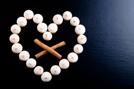Small cookies laid in the shape of heart and cinnamon on black background.の写真素材