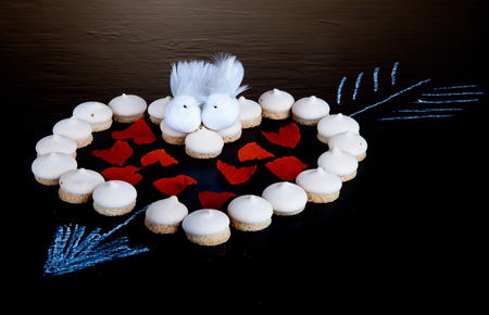 Small cookies laid in the shape of heart with arrow and paper hearts on black background.の写真素材