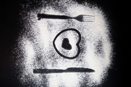 Silhouettes of fork, knife and hearts on the flour on a black background.の写真素材