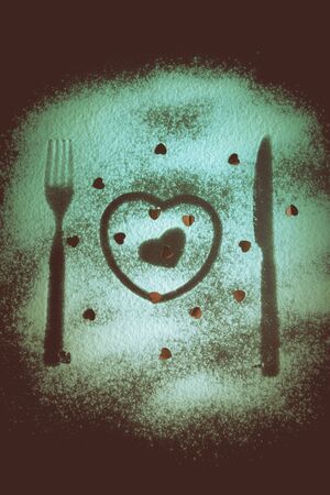 Silhouettes of fork, knife and hearts on the flour on a black background. Toned.の写真素材