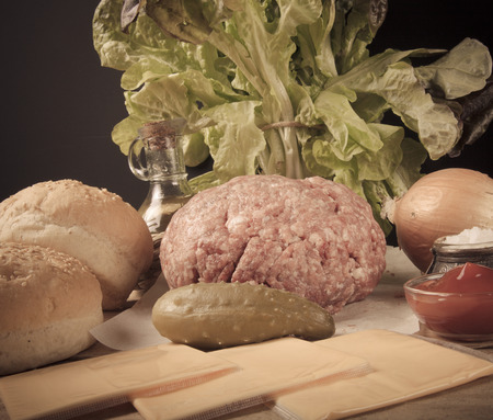 Meat, cheese, onions, herbs, salt, ketchup on a wooden table over black background. Ingredients for a hamburger. Toned.の写真素材