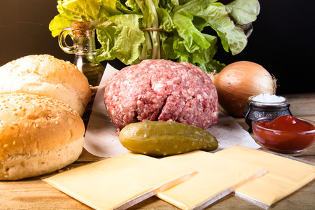 Meat, cheese, onions, herbs, salt, ketchup on a wooden table over black background. Ingredients for a hamburger. Toned.の写真素材
