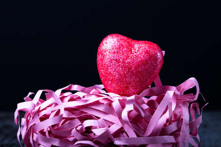 Shiny red heart with a paper straw on a black background.