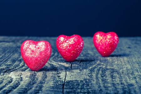 Three shiny red hearts on old wooden background. Toned.の写真素材