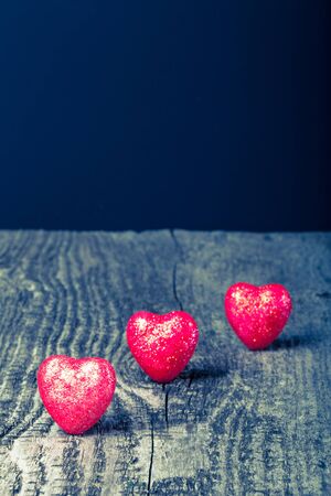 Three shiny red hearts on old wooden background. Toned.の写真素材