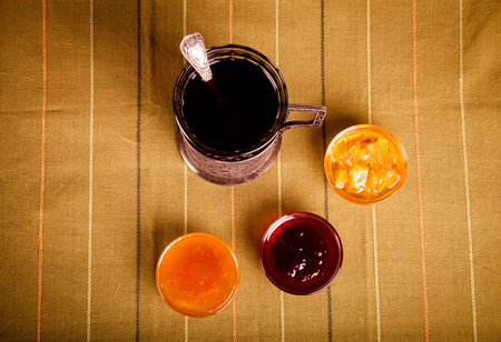 Tea in a glass with a cup holder, honey and jam on a green striped tablecloth. Toned.の写真素材