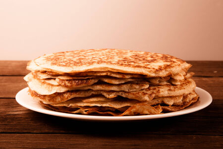 Stack of Russian pancakes - blini on a wite plate on old wooden table. Toned.