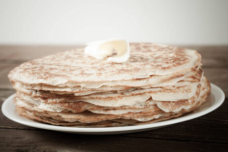 Stack of Russian pancakes - blini on a wite plate on old wooden table. Shallow depth of field.の写真素材