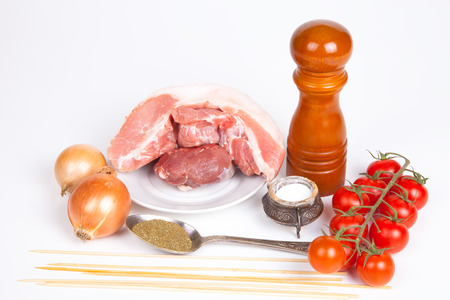 Raw meat, salt, pepper, tomatos, onion, spoon with herbs, sticks for barbecue. Still life on light background.の写真素材