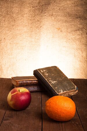 old books, apple and orange lying on an old wooden table.の写真素材