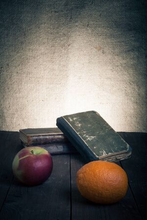 old books, apple and orange lying on an old wooden table.の写真素材